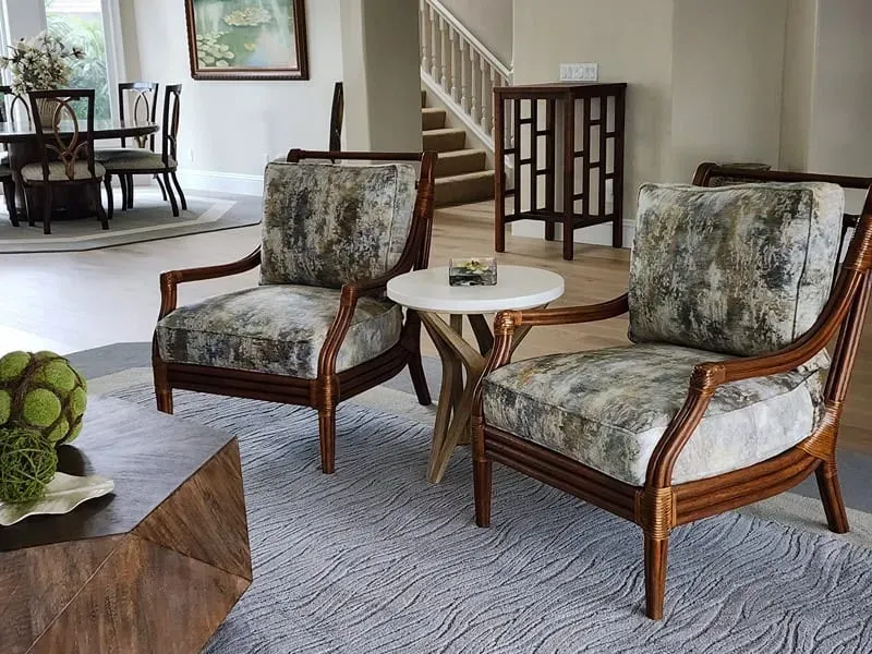 Two armchairs with patterned cushions sit near a small table on a light blue rug in a living room.