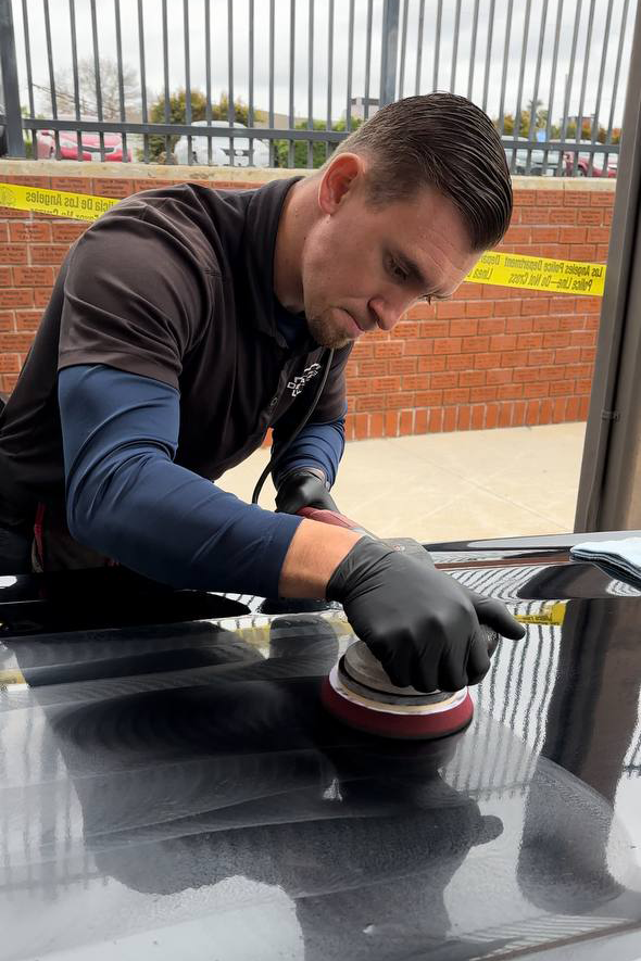 Man polishing a black car with a buffer, outdoors.