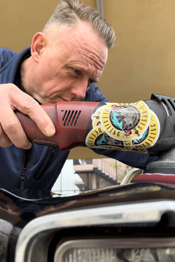 Man polishing a black car with a buffer. Outdoors; focused expression.