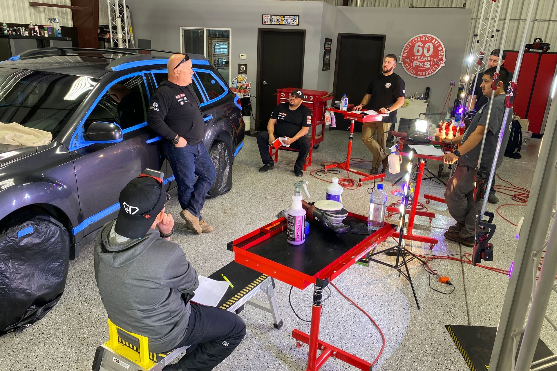 People in a car detailing workshop, focused on a car. Several are working, others observing.