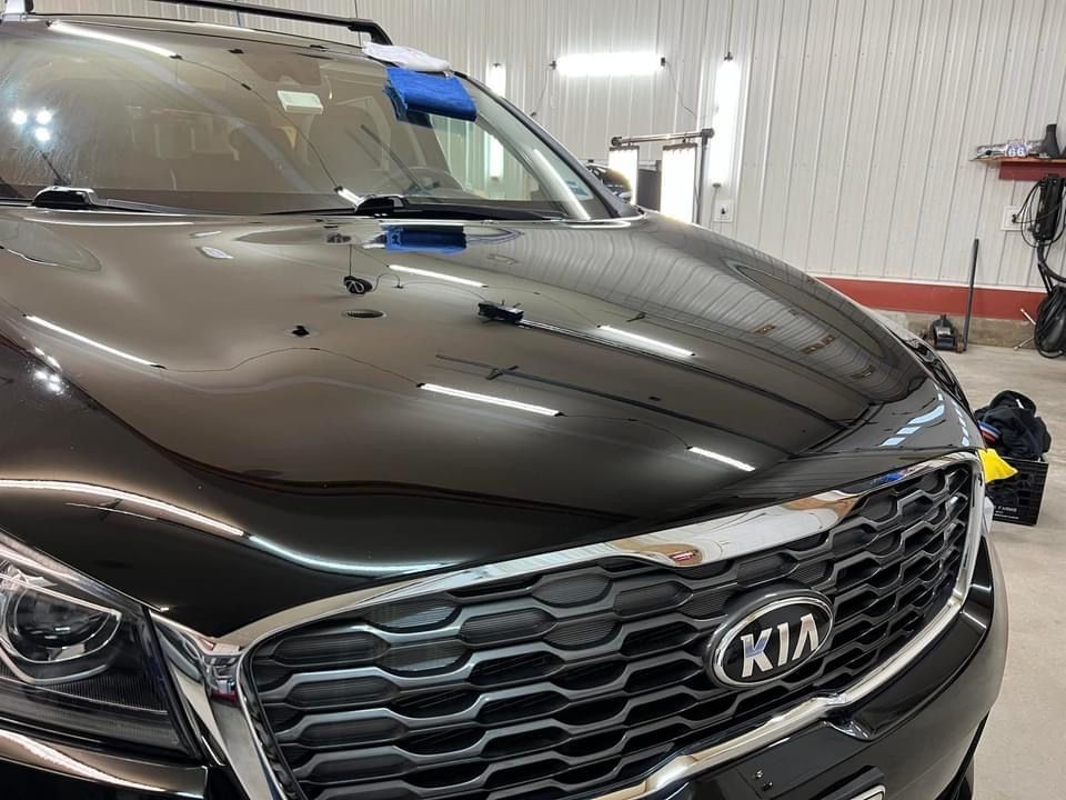 Black Kia SUV hood reflecting the interior of a detail shop.
