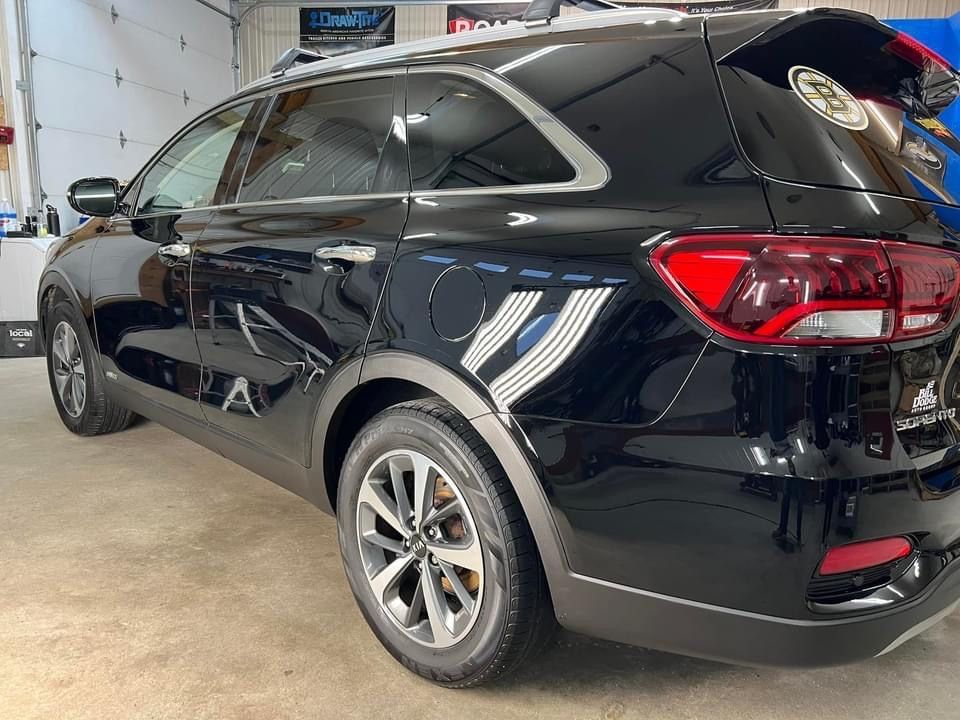 Black Kia Sorento SUV in a garage, shiny paint, silver wheels, parked indoors.