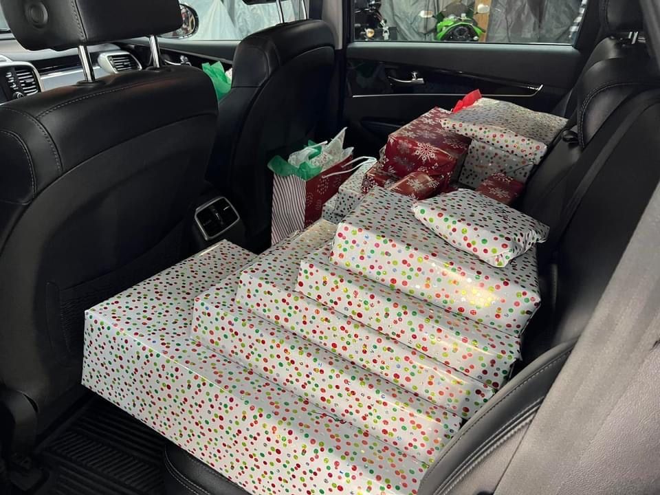 Rear car seat filled with wrapped gifts; various sizes, patterns, and colors.