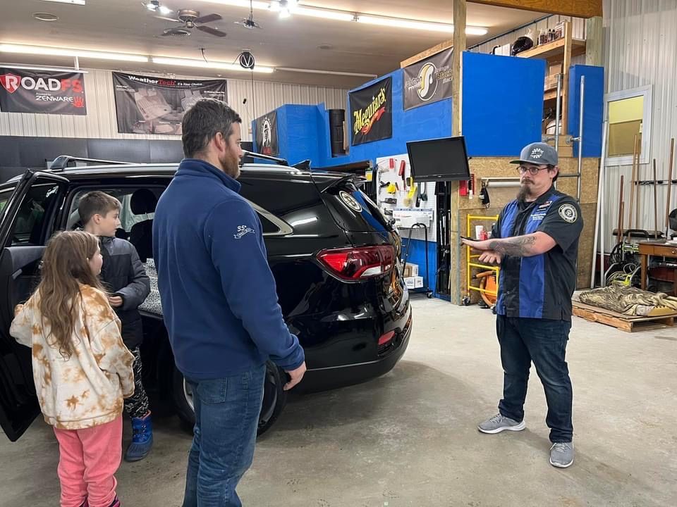 A mechanic showing a car to a family in a garage. The car is black and the mechanic is gesturing.