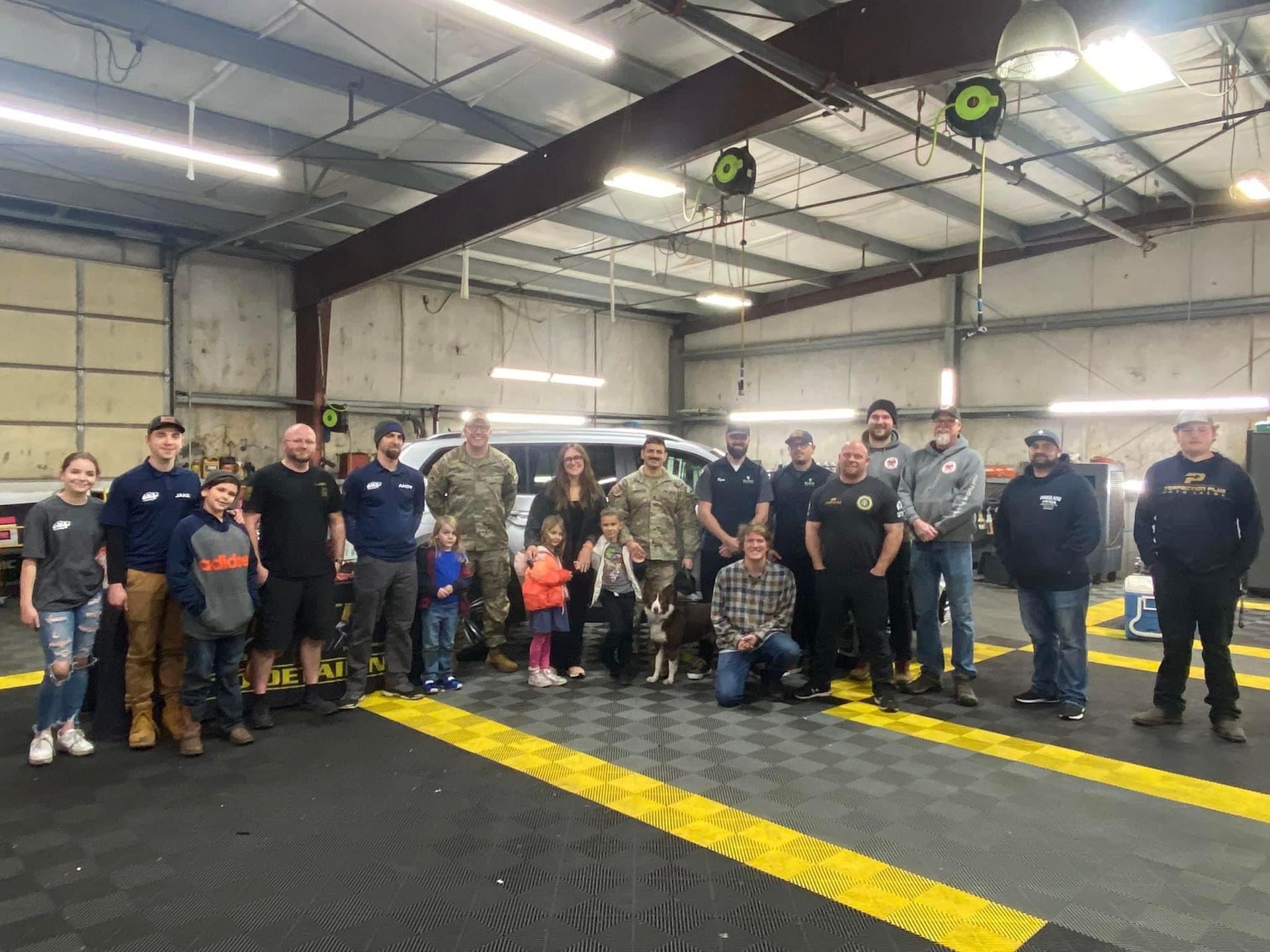 Group of people pose in a garage with a van; includes children, military members, and first responders.