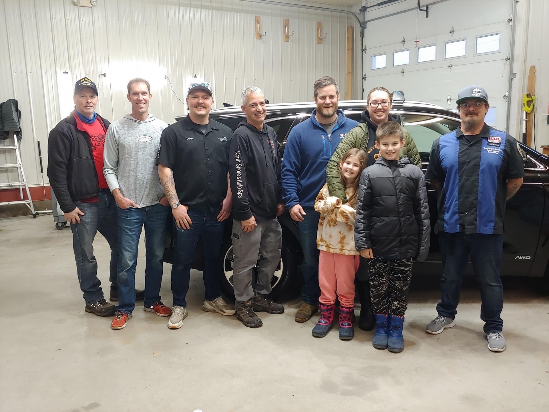 Group of men and two children pose in front of a car in a garage.