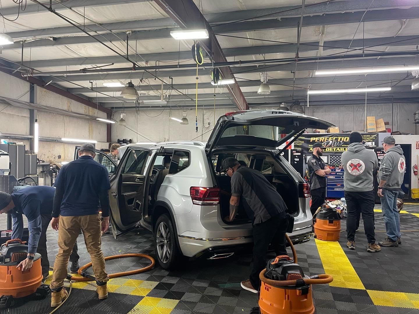 A group of people working inside a car repair shop, working on a silver SUV.