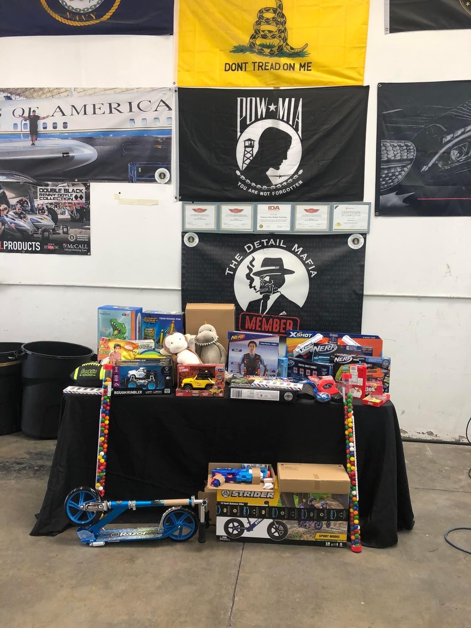 A table displays various toys and gifts, set against a backdrop of flags, including a Gadsden flag.