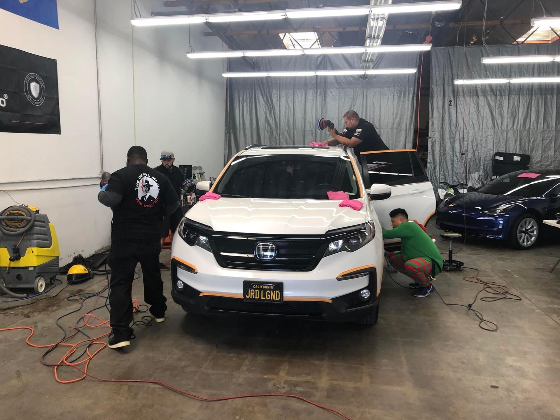 People working on a white SUV in a garage. Men are cleaning and detailing the vehicle.