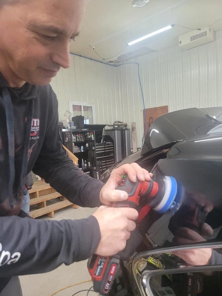 Man polishing a black car with a red and black polisher. Indoors, garage setting.