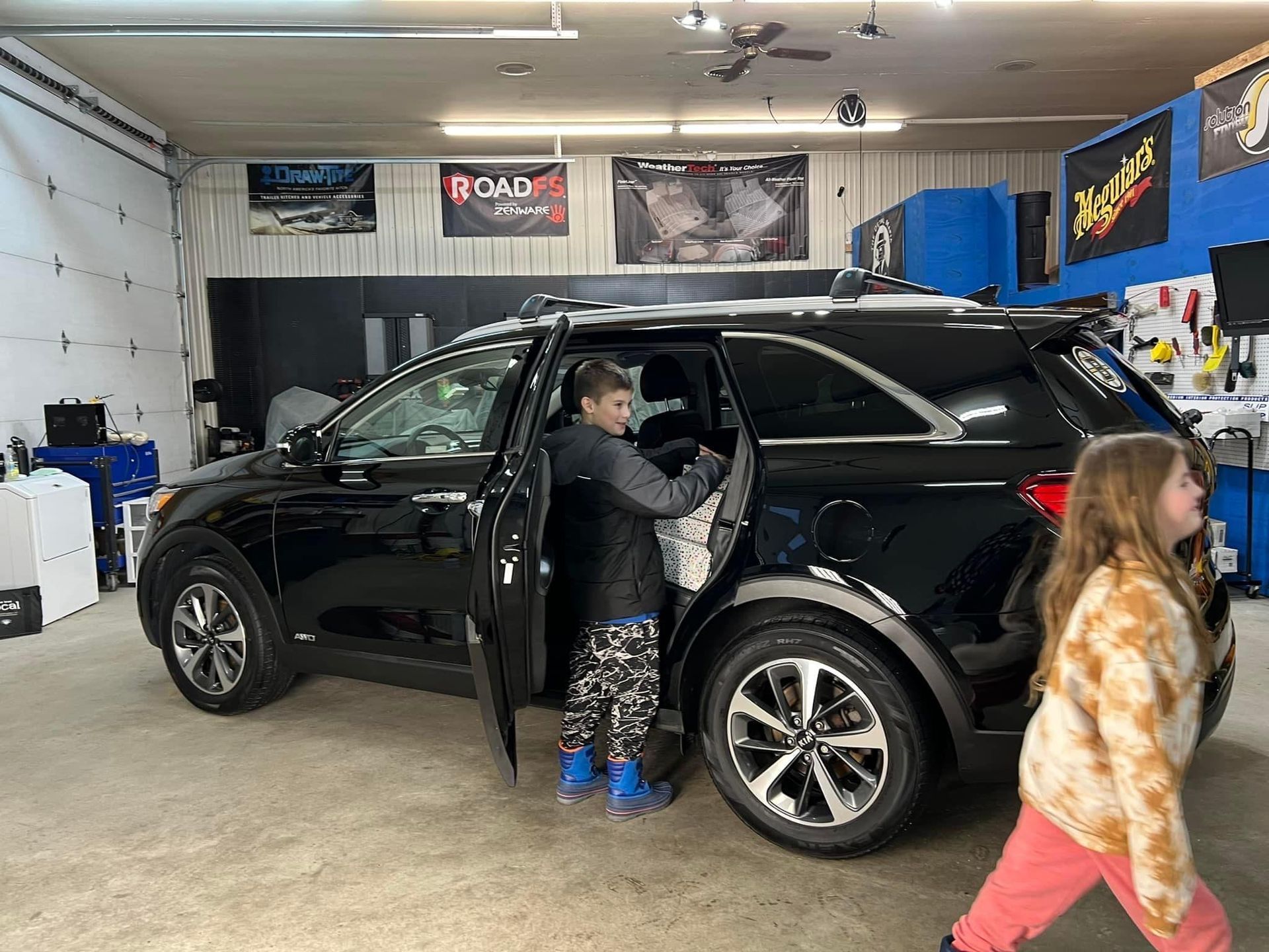 Black SUV with a child entering and another walking by in a garage.