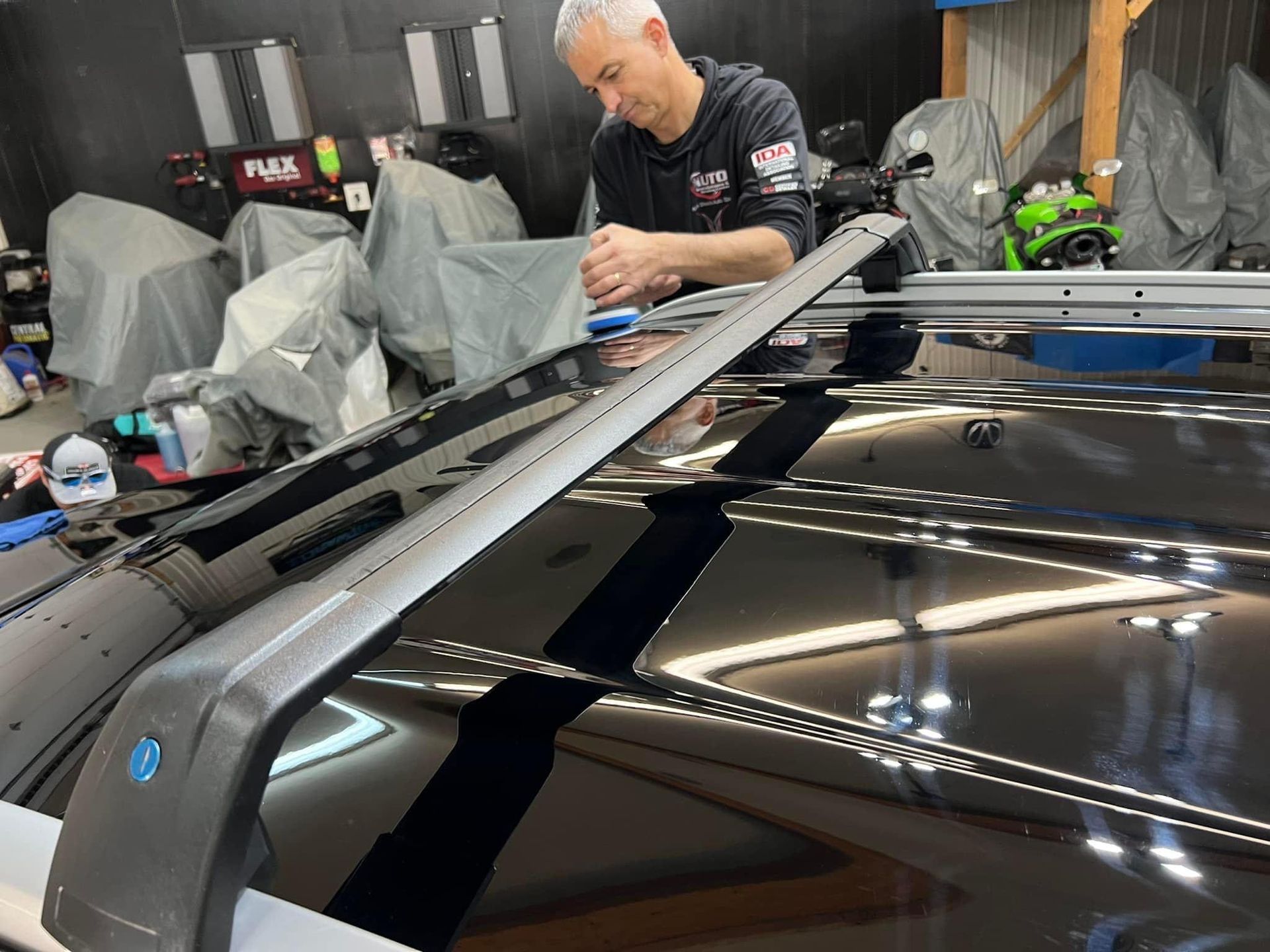 Man working on a car roof with a rack, indoors. Shiny black car, silver rack, man in black shirt.