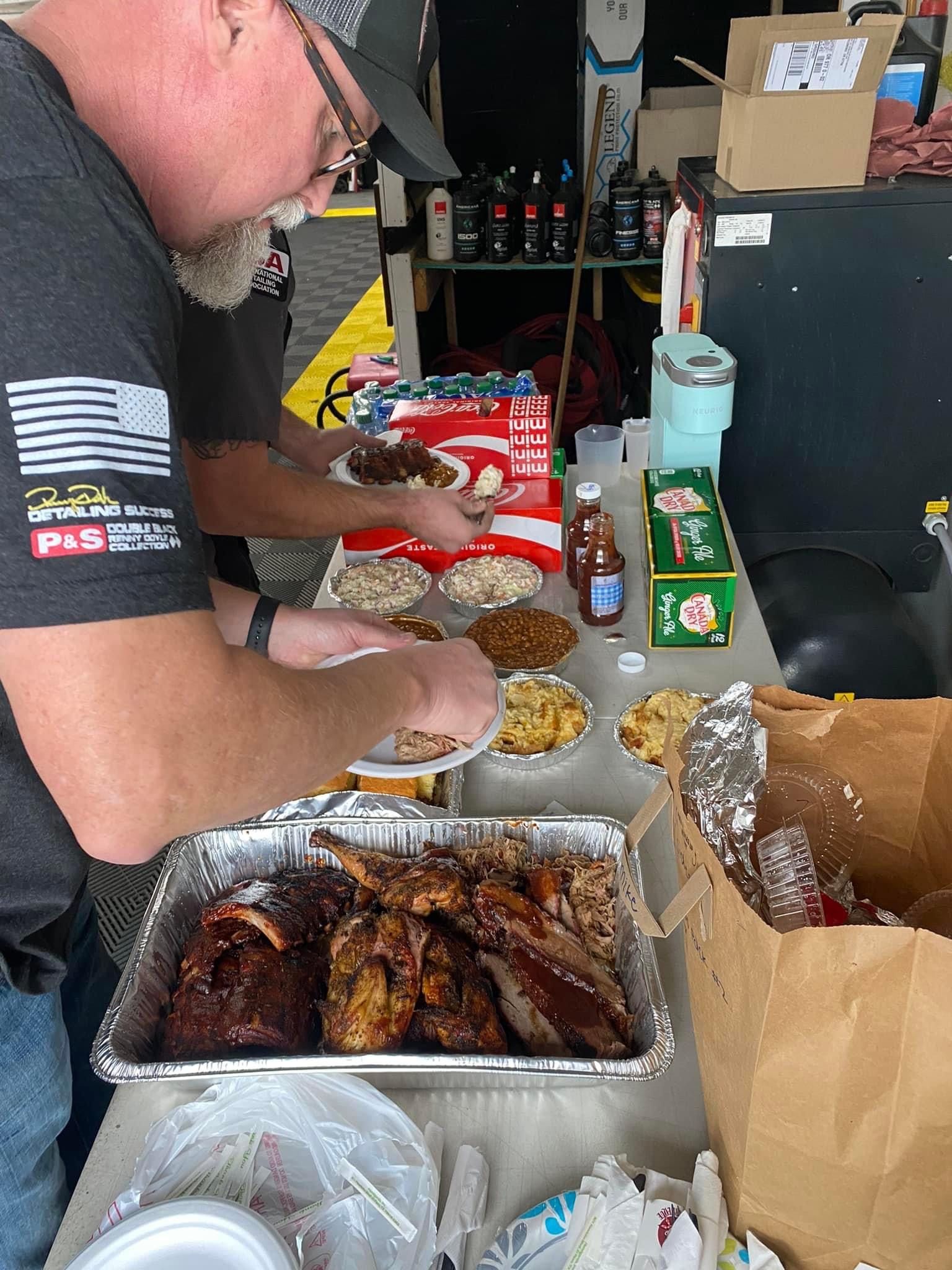 Man serving BBQ ribs, sides like mac & cheese, beans, and drinks at an outdoor cookout.