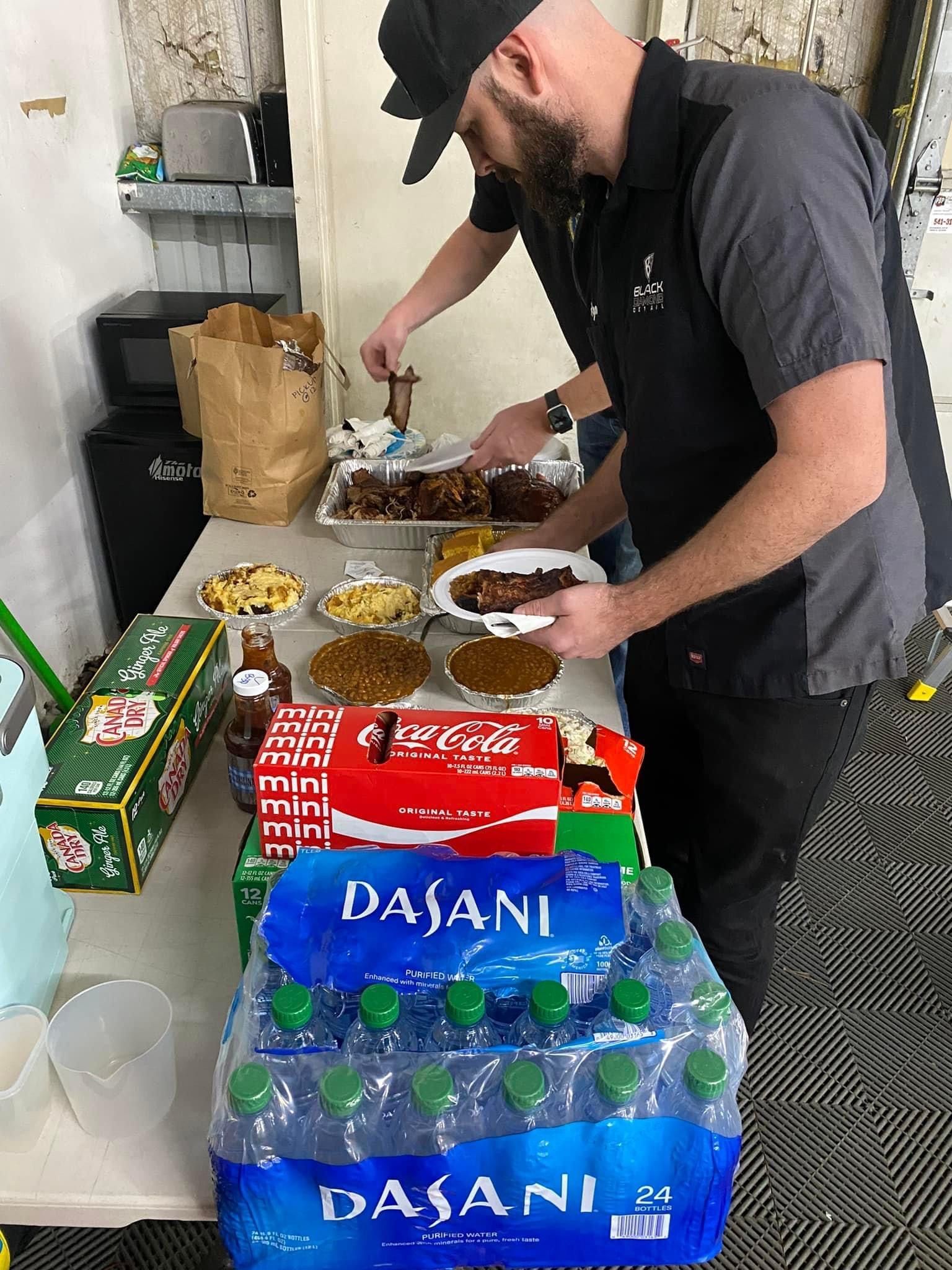 Two men serving food from a table. Food items include meat, rice, and sides. Drinks and condiments are also present.