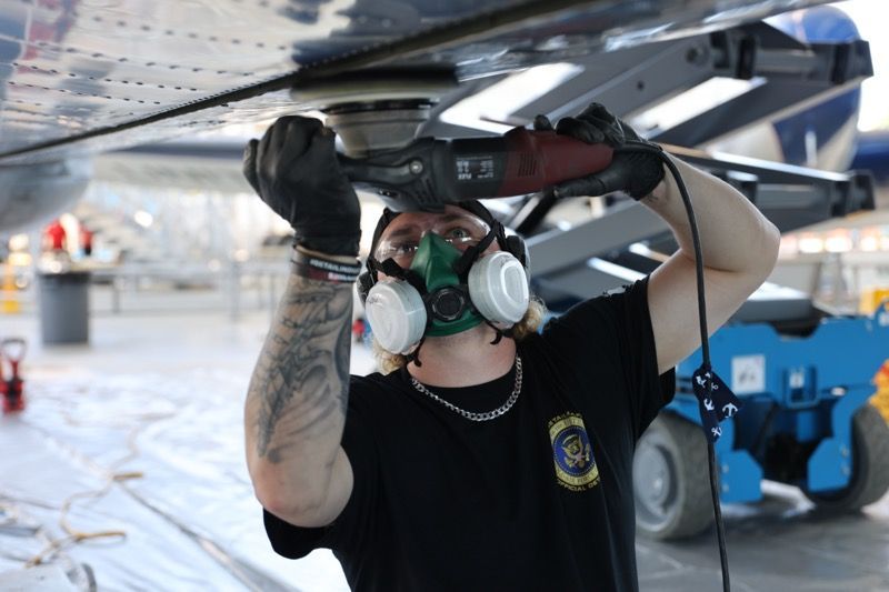 Mechanic grinding on aircraft wing while wearing a respirator. Hangar setting.