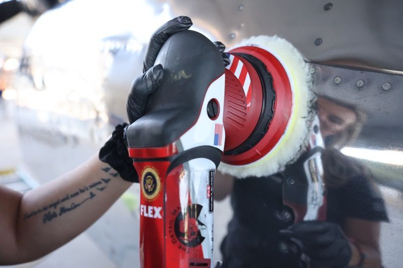 Person polishing metal surface with red and black electric polisher.