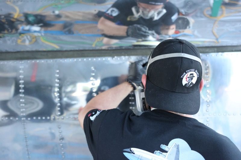 Person in black shirt and cap sanding metal, likely aircraft repair.