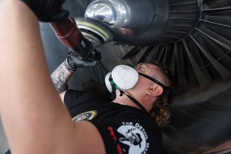 Man polishing a jet engine, wearing a mask, in a hangar.