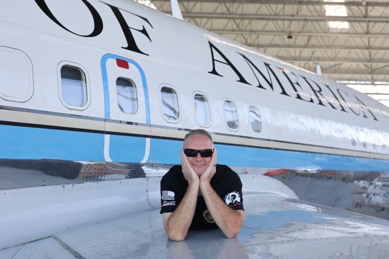 Man in sunglasses poses on wing of an airplane painted 