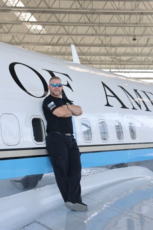 Man in sunglasses leans against an airplane wing, arms crossed, near 