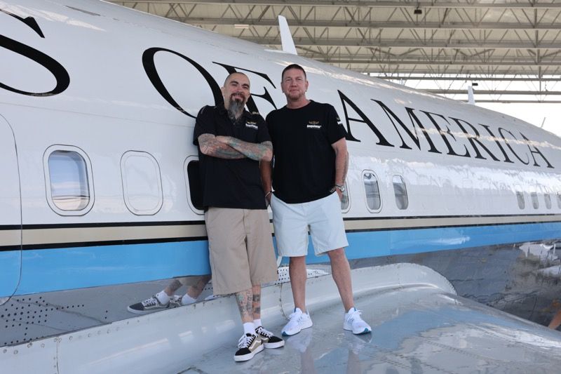 Two men stand by a white airplane with 