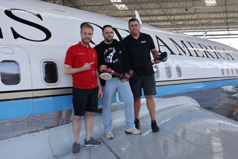 Three men standing near a white airplane with “UNITED STATES OF AMERICA” painted on it.
