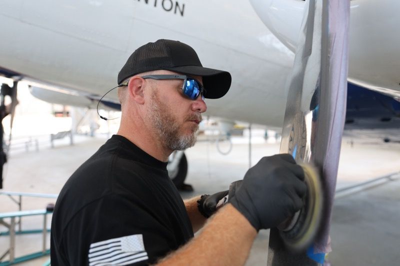 Man in cap and sunglasses sanding an airplane wing.