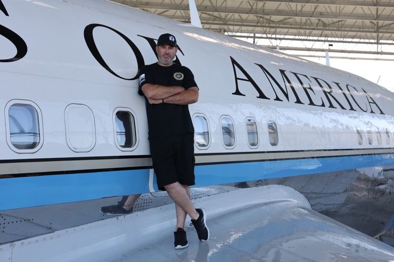 Man in black leaning against a plane labeled 