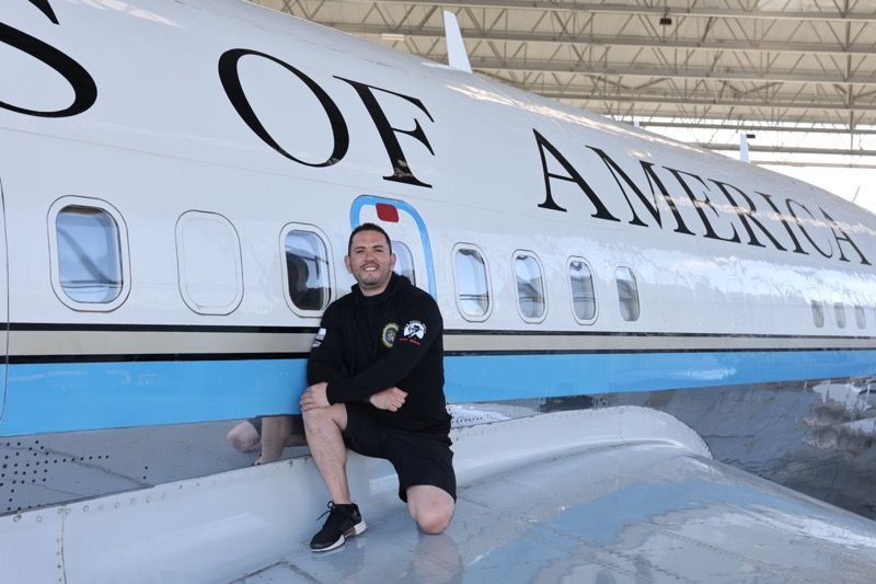 Man kneels on an aircraft wing in front of a plane labeled 