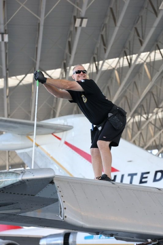 Man on airplane wing, holding pole, stretching. In hangar, United plane.
