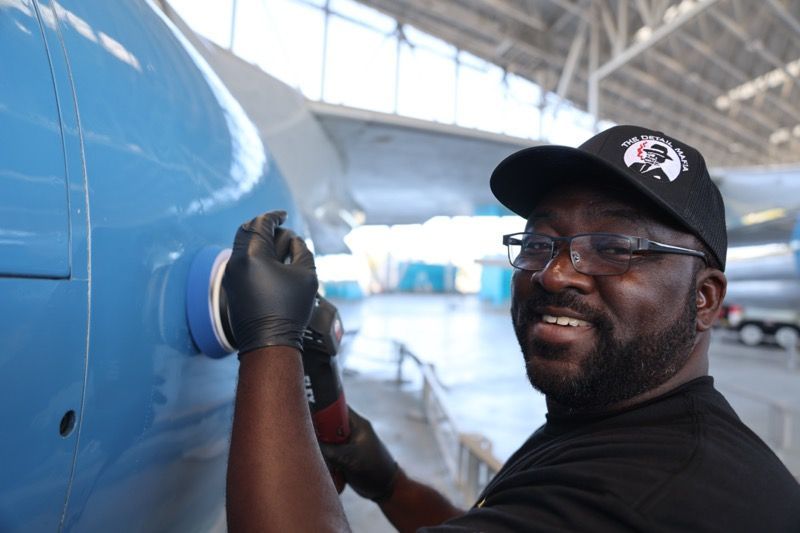 Smiling man in cap and gloves tapes blue plane, inside a hangar.
