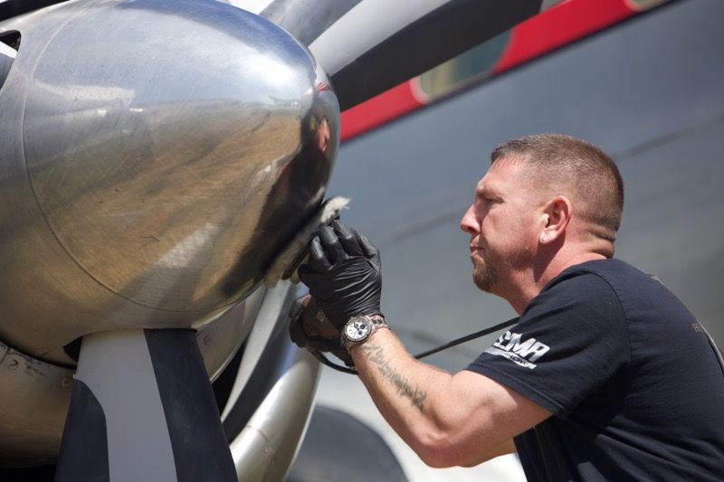 Man in black gloves polishing the silver hub of an airplane propeller.