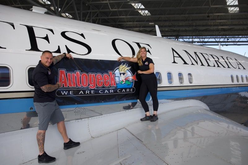 Two people pose with a banner in front of an airplane that says 