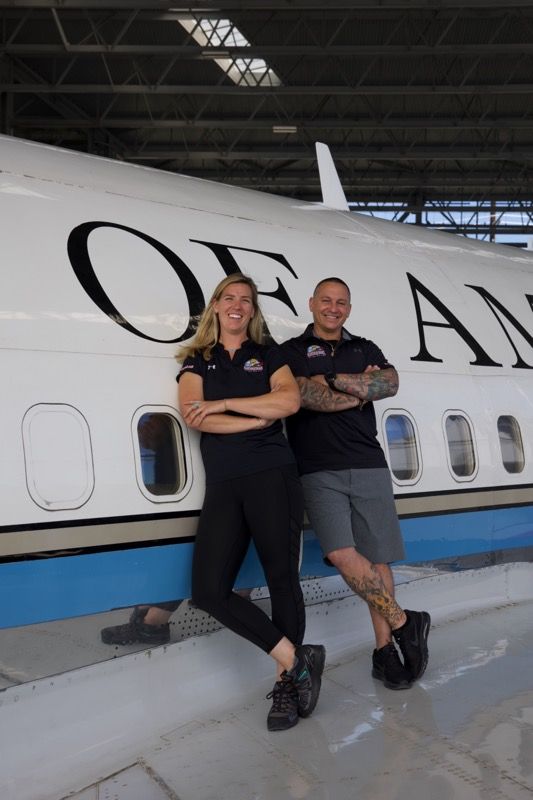 Two people pose beside a white plane that reads 