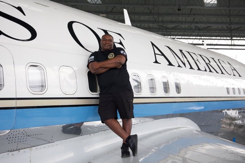 Man leaning against the side of a plane that reads 