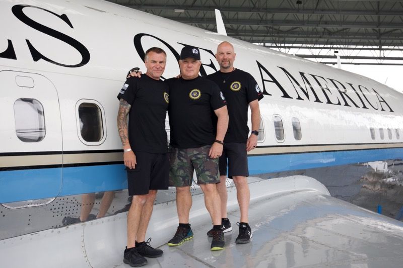 Three men pose in front of a plane labeled 