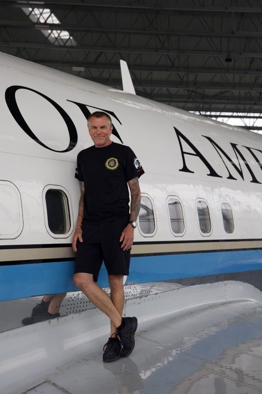 Man in black leans against a plane labeled 