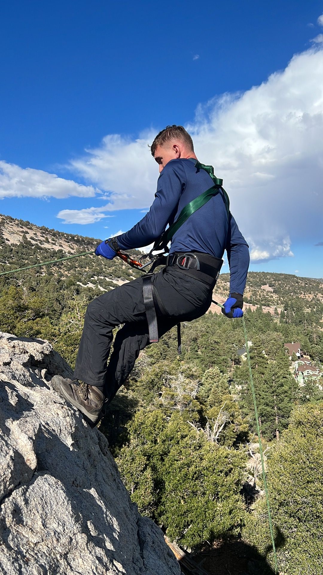 Man rappelling down a rocky cliff face, wearing safety gear, against a blue sky.