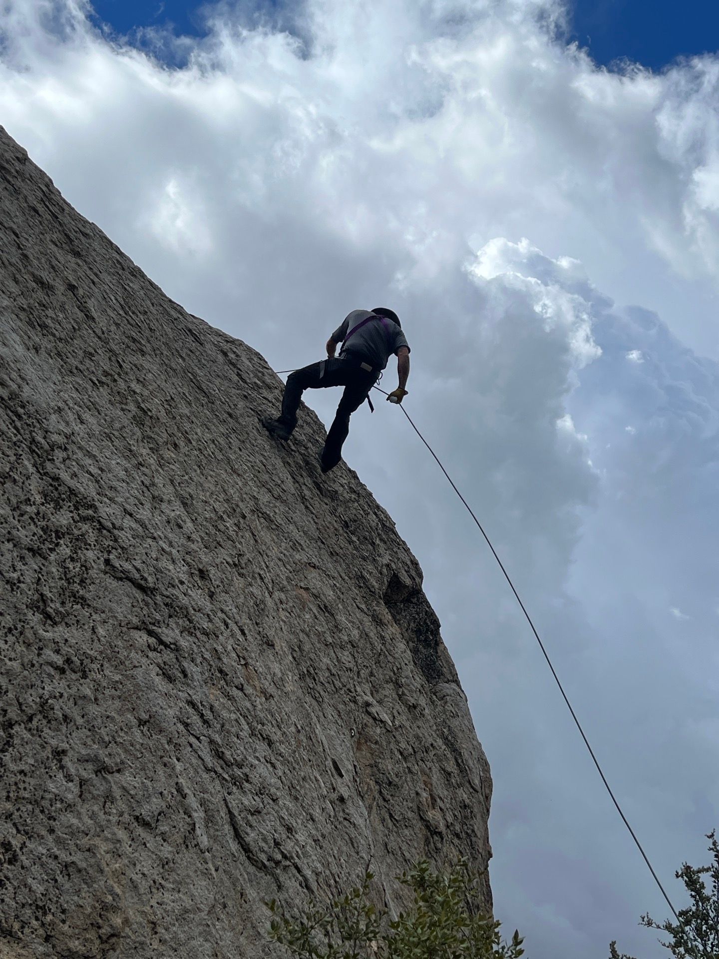 Rock climber rappels down a steep rock face against a cloudy blue sky.