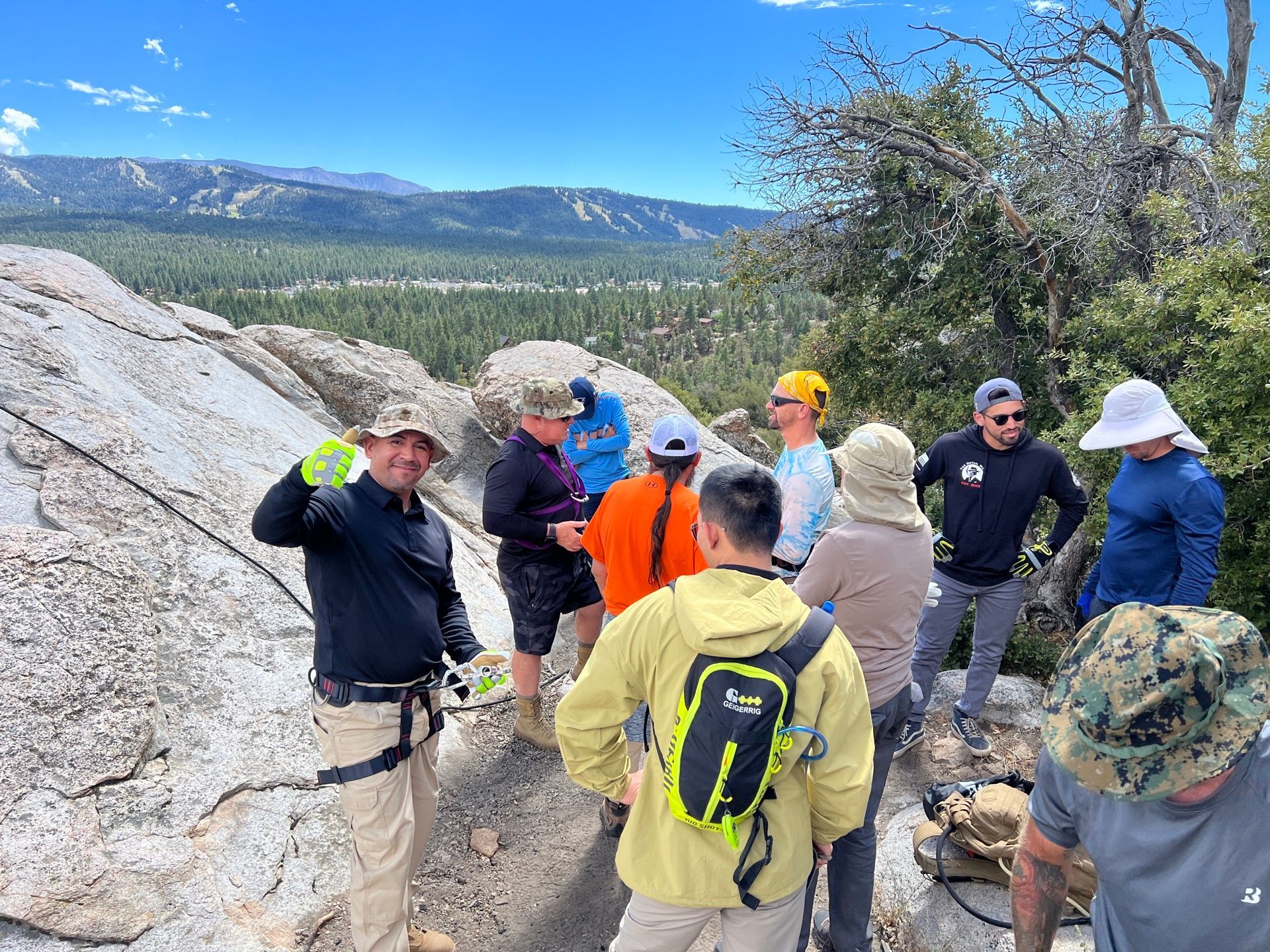 Group of people on a rocky mountaintop. One person gestures. Scenic mountain landscape in background.