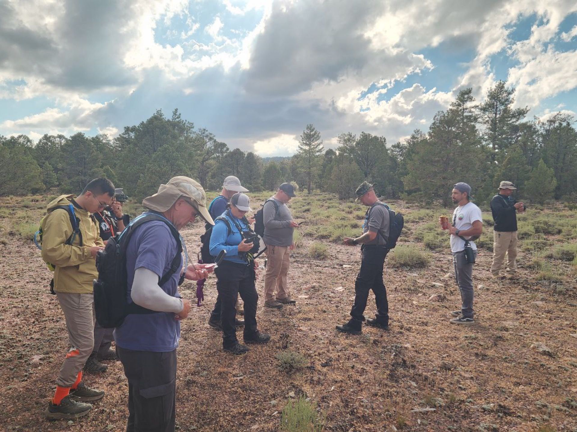 Group of people surveying terrain, outdoors, under cloudy skies.