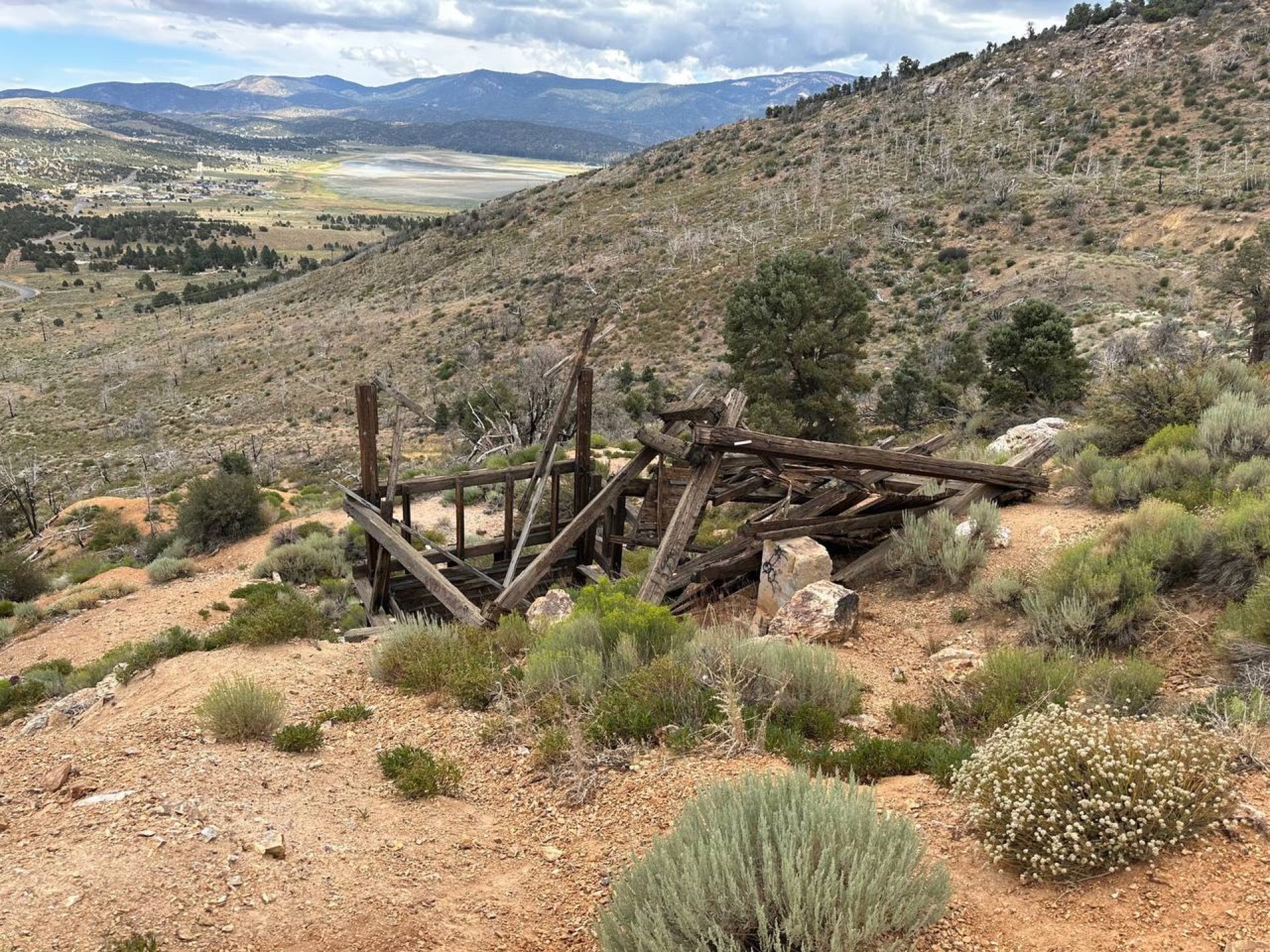 Dilapidated wooden structure on a hillside overlooking a valley. Overcast sky, brown/green landscape.