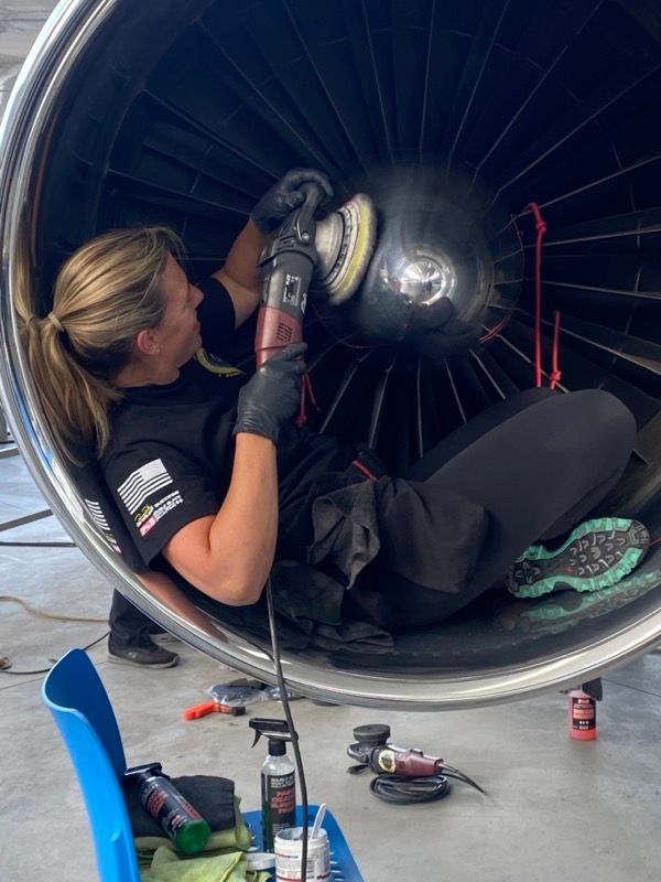 Woman polishing an aircraft engine with a power buffer. Inside engine, she sits with black gloves and clothing.