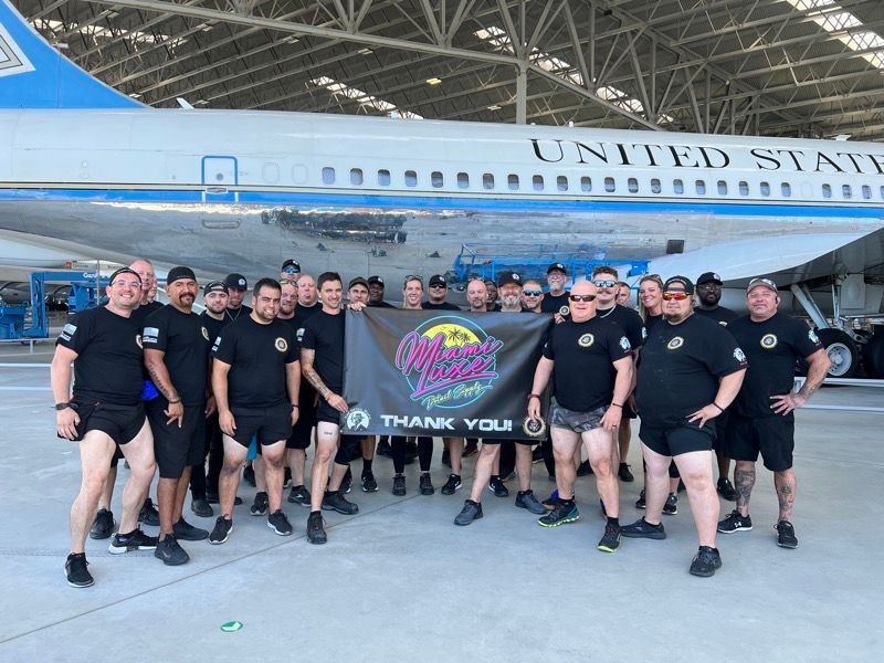 Group of men in black shorts and shirts holding a banner in front of a plane labeled 