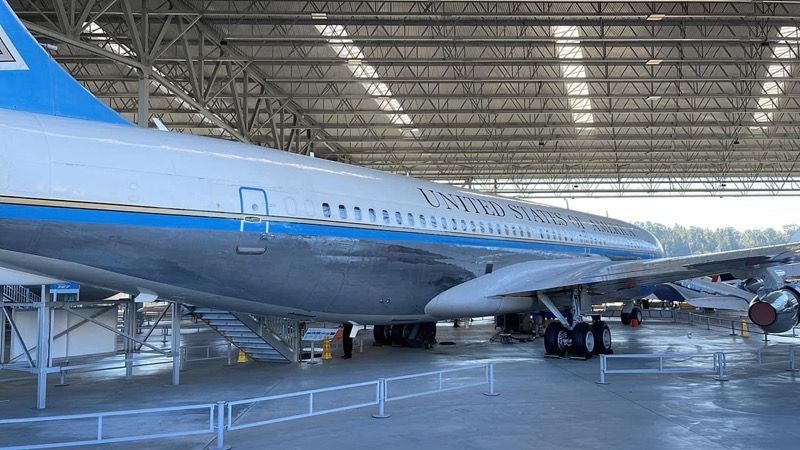 Air Force One (Boeing 707) in a hangar. White fuselage, blue stripes, and 