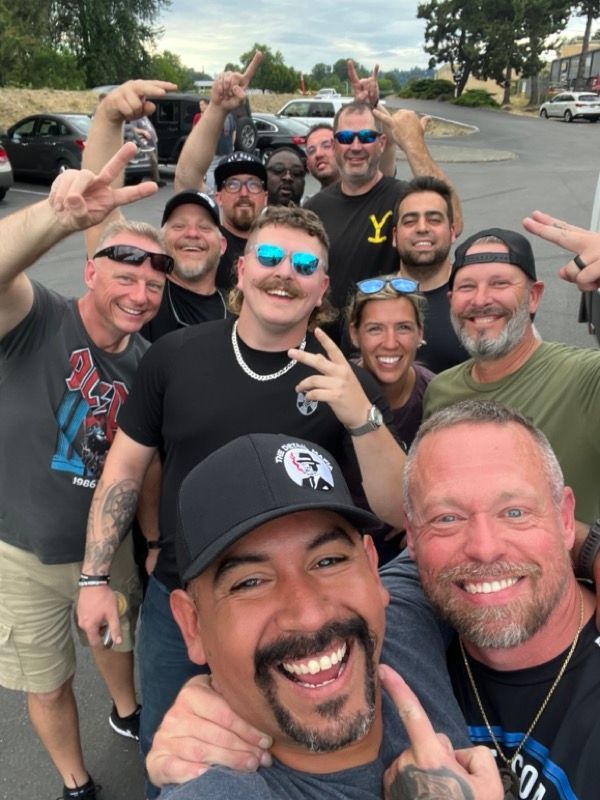 Group of people smiling for selfie outdoors, making hand gestures.