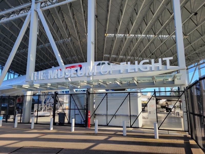 The Museum of Flight entrance with white sign and large aircraft under a steel structure.