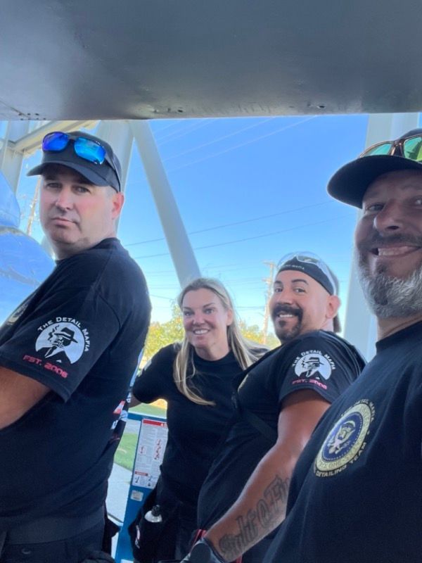 Four people smiling, wearing black shirts and hats, positioned in a white structure, with a blue sky backdrop.