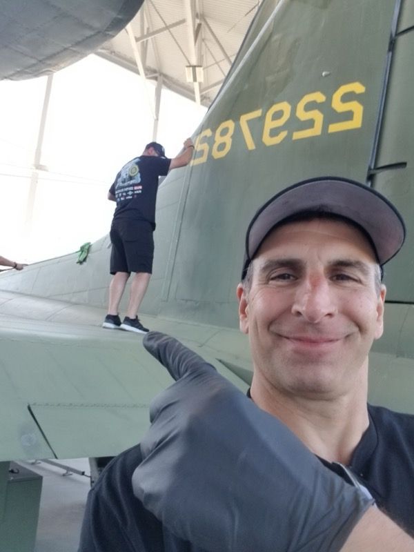 Man pointing at a plane's tail where another person is painting. The tail has yellow text on a green surface.