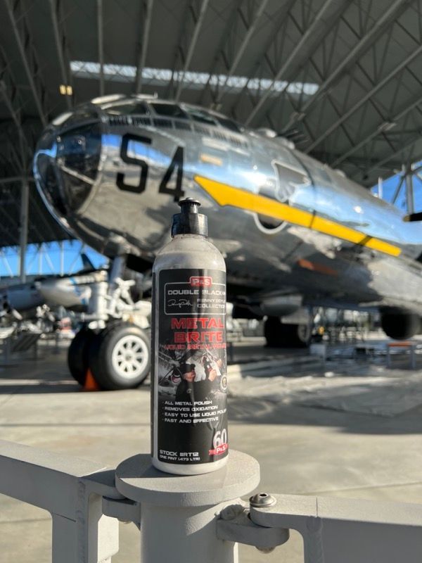 Bottle of car detailing product in front of a silver B-29 bomber in a hangar.